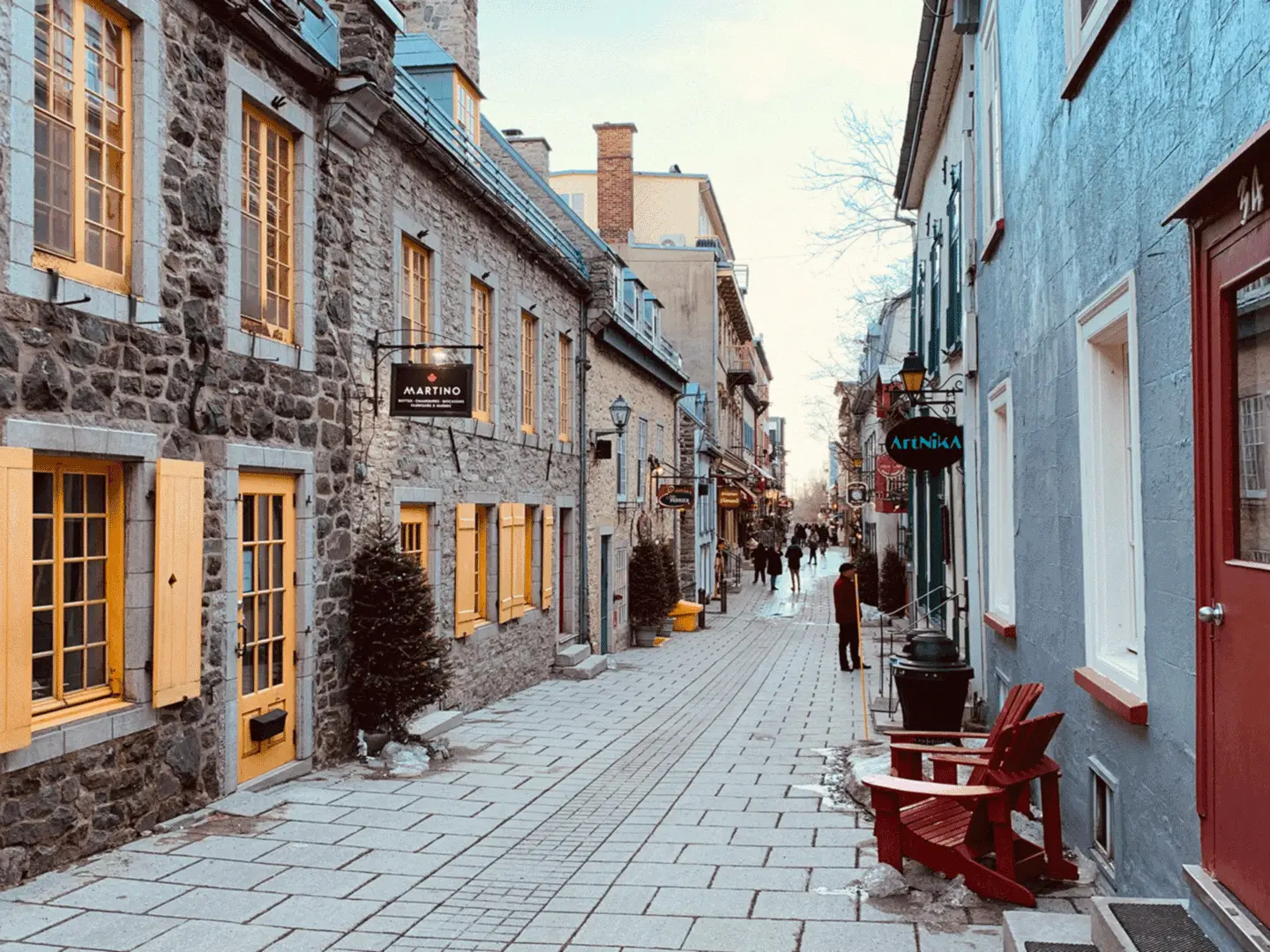 Charming cobblestone street in Old Quebec lined with stone buildings, colorful shutters, boutique shops, and pedestrians exploring the area.